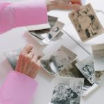 An elderly woman in a pink shirt sorting through old black and white family photographs, evoking nostalgia.